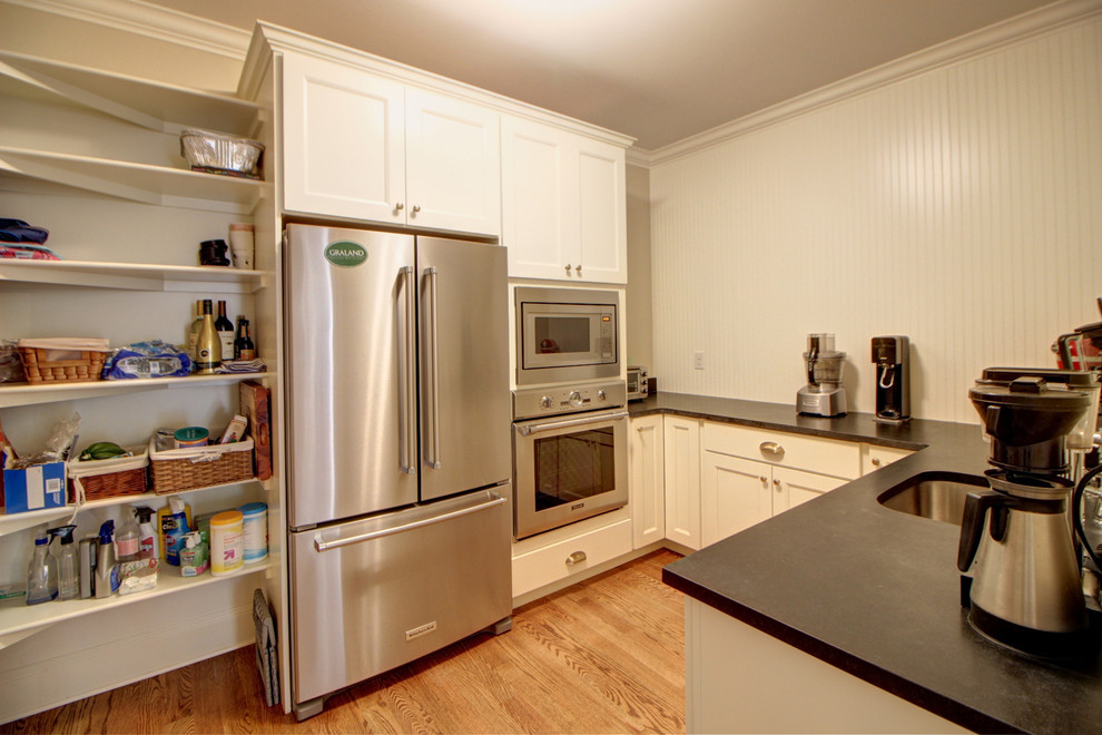 Large transitional l-shaped medium tone wood floor kitchen pantry photo in Denver with a farmhouse sink, raised-panel cabinets, white cabinets, soapstone countertops, stainless steel appliances and an island