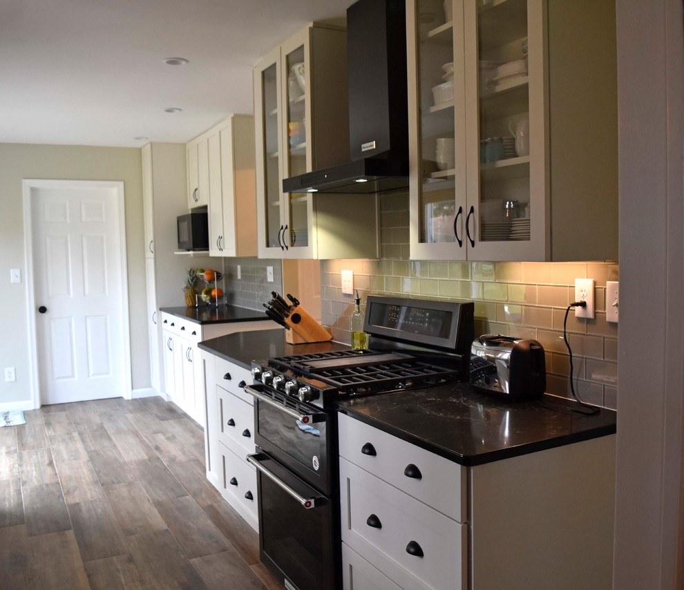 Inspiration for a mid-sized transitional galley laminate floor and brown floor enclosed kitchen remodel in DC Metro with a farmhouse sink, shaker cabinets, white cabinets, granite countertops, gray backsplash, subway tile backsplash, stainless steel appliances, no island and black countertops