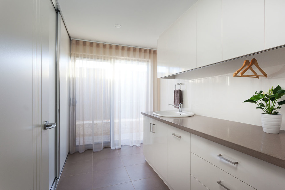 Traditional single-wall dedicated laundry room in Perth with a drop-in sink, white cabinets, solid surface benchtops, beige walls, ceramic floors, grey floor and brown benchtop.