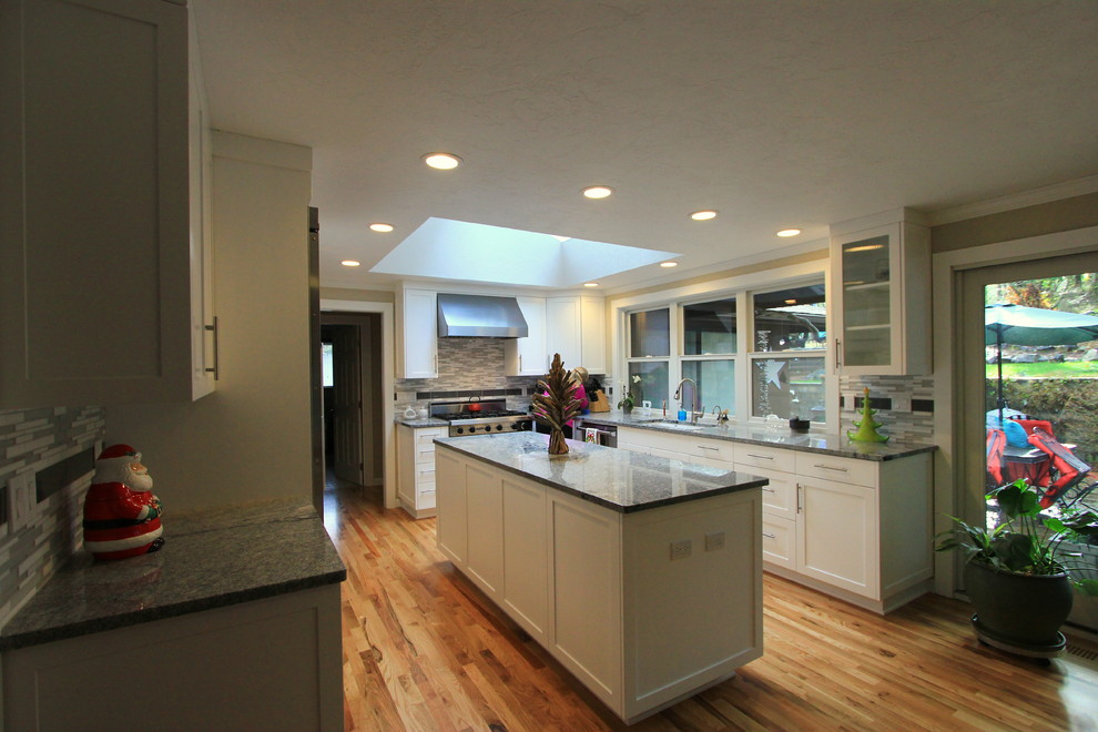 Example of a large transitional u-shaped light wood floor open concept kitchen design with an undermount sink, shaker cabinets, white cabinets, granite countertops, multicolored backsplash, mosaic tile backsplash, stainless steel appliances and an island