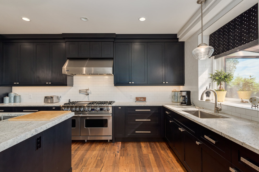 Inspiration for a transitional u-shaped medium tone wood floor and brown floor kitchen remodel in Calgary with an undermount sink, shaker cabinets, black cabinets, quartz countertops, white backsplash, ceramic backsplash, stainless steel appliances and an island