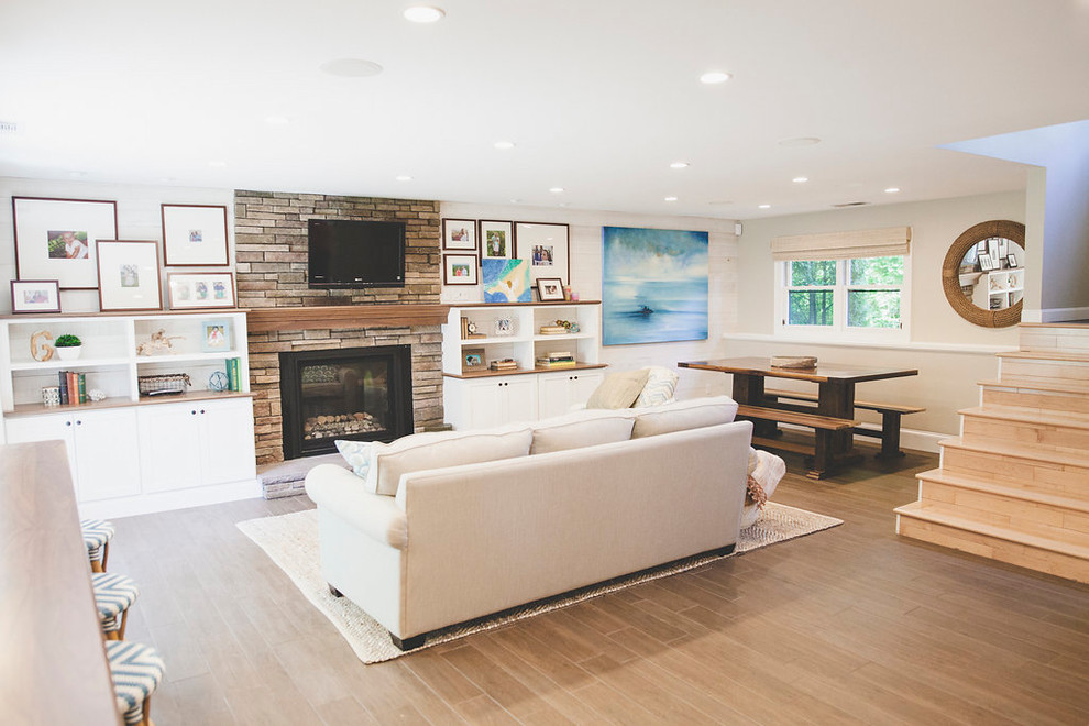 This is an example of a mid-sized beach style open concept family room in Providence with a home bar, white walls, porcelain floors, a standard fireplace, a stone fireplace surround, a wall-mounted tv and brown floor.