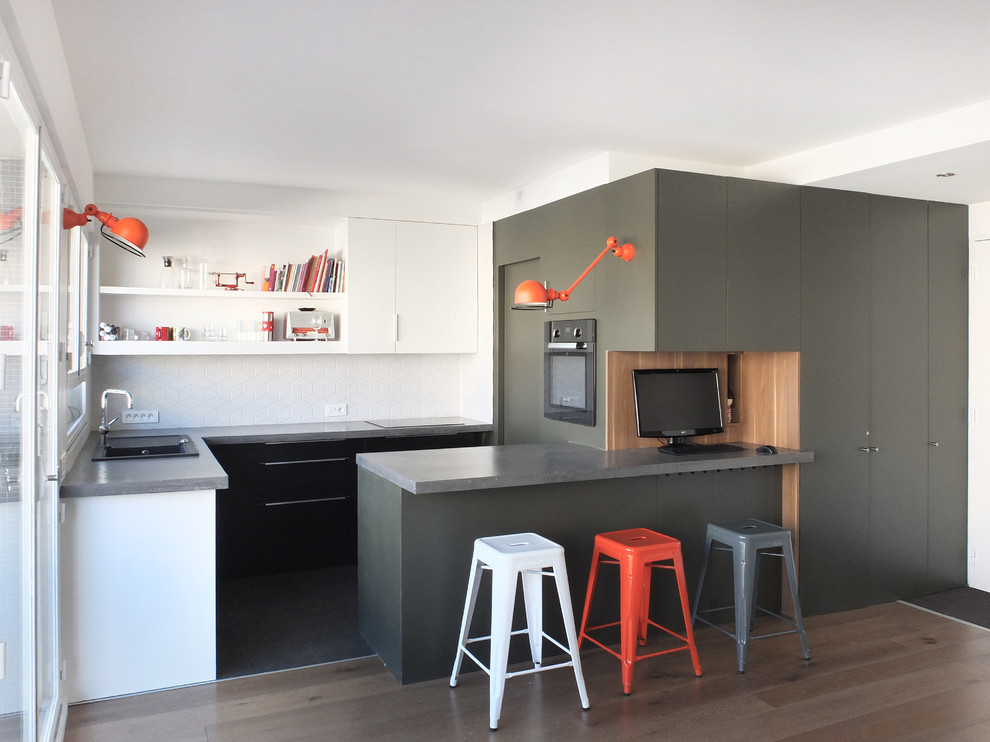 Inspiration for a mid-sized contemporary u-shaped open plan kitchen in Paris with flat-panel cabinets, white splashback, a peninsula, a drop-in sink, black cabinets, concrete benchtops, ceramic splashback and panelled appliances.