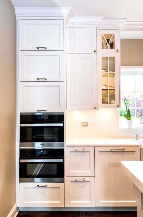 Example of a mid-sized transitional single-wall dark wood floor enclosed kitchen design with a farmhouse sink, shaker cabinets, white cabinets, white backsplash, stainless steel appliances and an island