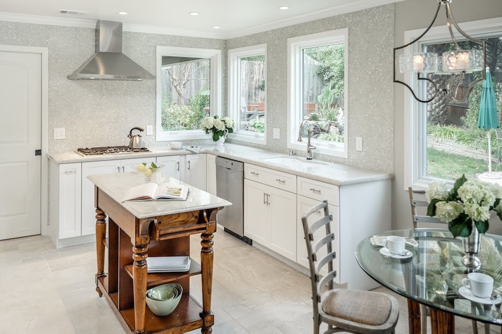 Example of a large transitional u-shaped limestone floor eat-in kitchen design with an undermount sink, shaker cabinets, white cabinets, marble countertops, metallic backsplash, mosaic tile backsplash, stainless steel appliances and an island