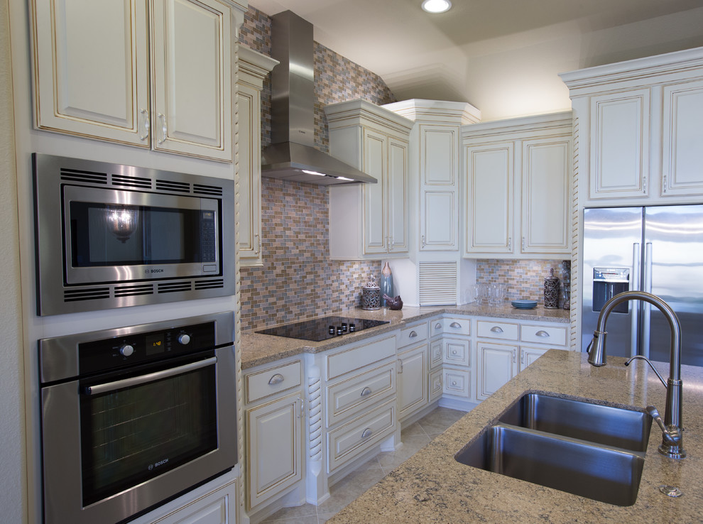 This is an example of a mid-sized traditional l-shaped separate kitchen in Austin with a double-bowl sink, raised-panel cabinets, white cabinets, quartzite benchtops, multi-coloured splashback, mosaic tile splashback, stainless steel appliances, ceramic floors, with island and beige floor.