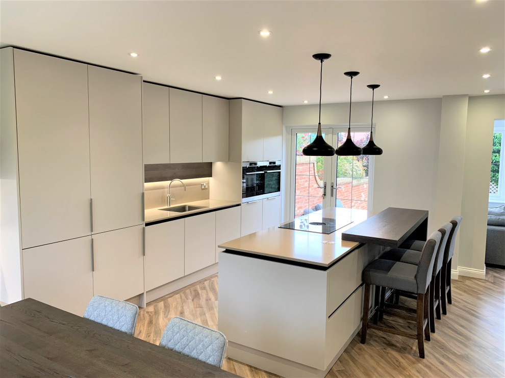 Photo of a mid-sized contemporary single-wall eat-in kitchen in Other with a single-bowl sink, flat-panel cabinets, medium wood cabinets, solid surface benchtops, engineered quartz splashback, black appliances, vinyl floors, with island and beige benchtop.