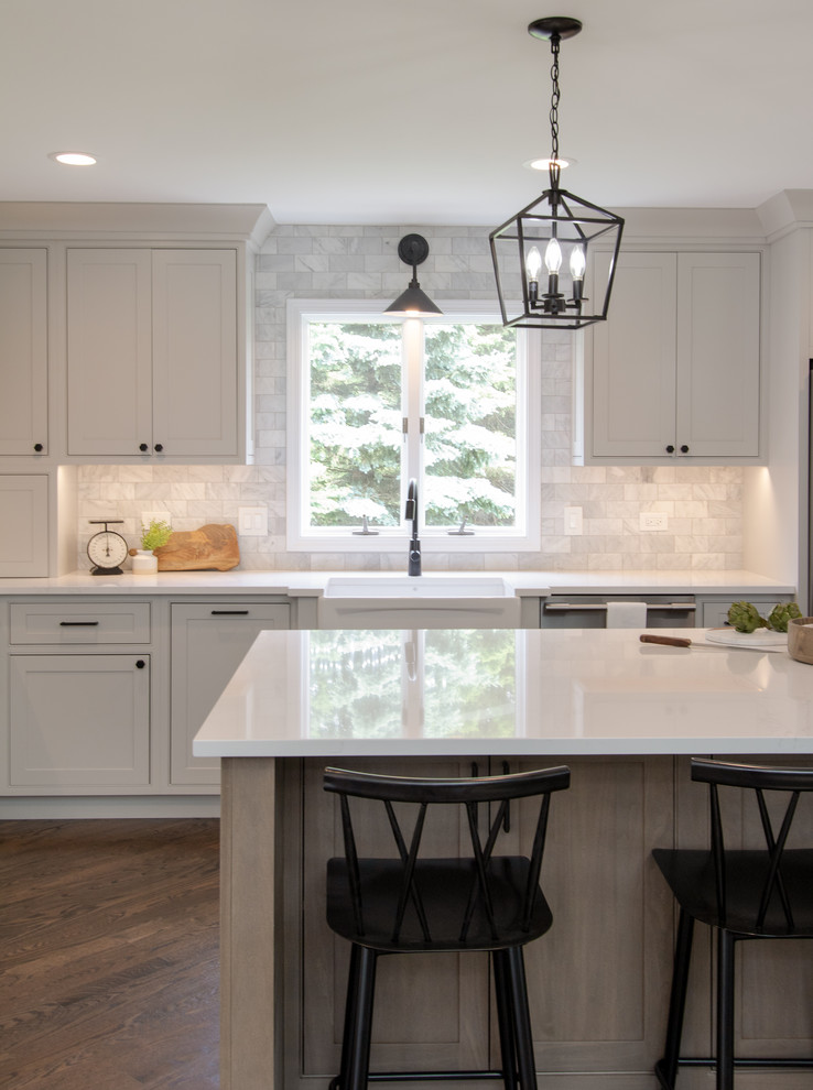 This is an example of a country l-shaped open plan kitchen in Chicago with a farmhouse sink, beaded inset cabinets, grey cabinets, quartz benchtops, marble splashback, stainless steel appliances, dark hardwood floors, with island and white benchtop.