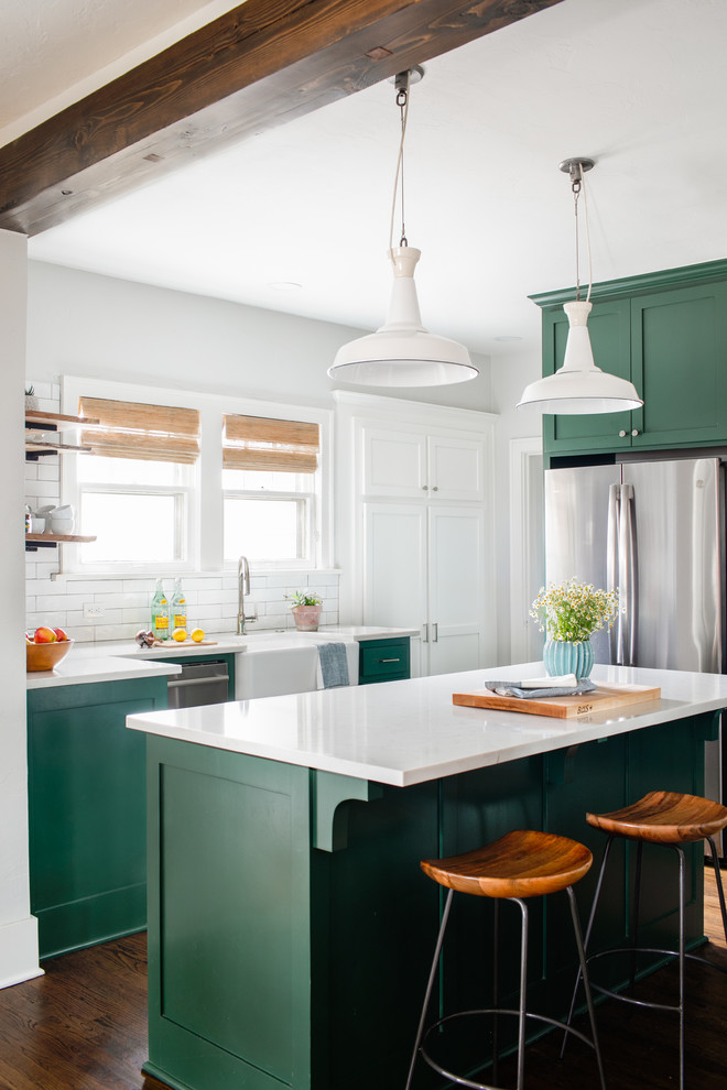 Design ideas for a mid-sized transitional kitchen in Chicago with a farmhouse sink, shaker cabinets, green cabinets, quartz benchtops, white splashback, subway tile splashback, stainless steel appliances, medium hardwood floors, with island, brown floor and white benchtop.