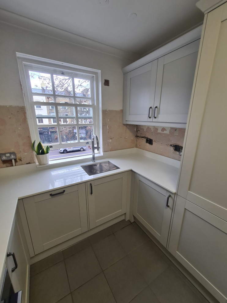 Photo of a mid-sized traditional u-shaped separate kitchen in London with an integrated sink, shaker cabinets, white cabinets, quartzite benchtops, white splashback, engineered quartz splashback, panelled appliances, ceramic floors, grey floor and white benchtop.