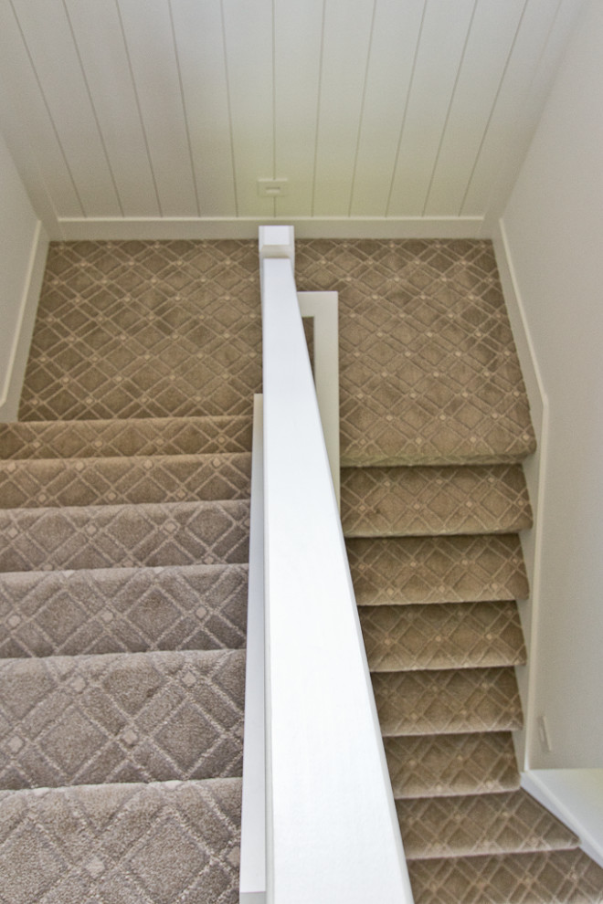 This is an example of a country carpeted u-shaped staircase in Other with carpet risers, wood railing and decorative wall panelling.