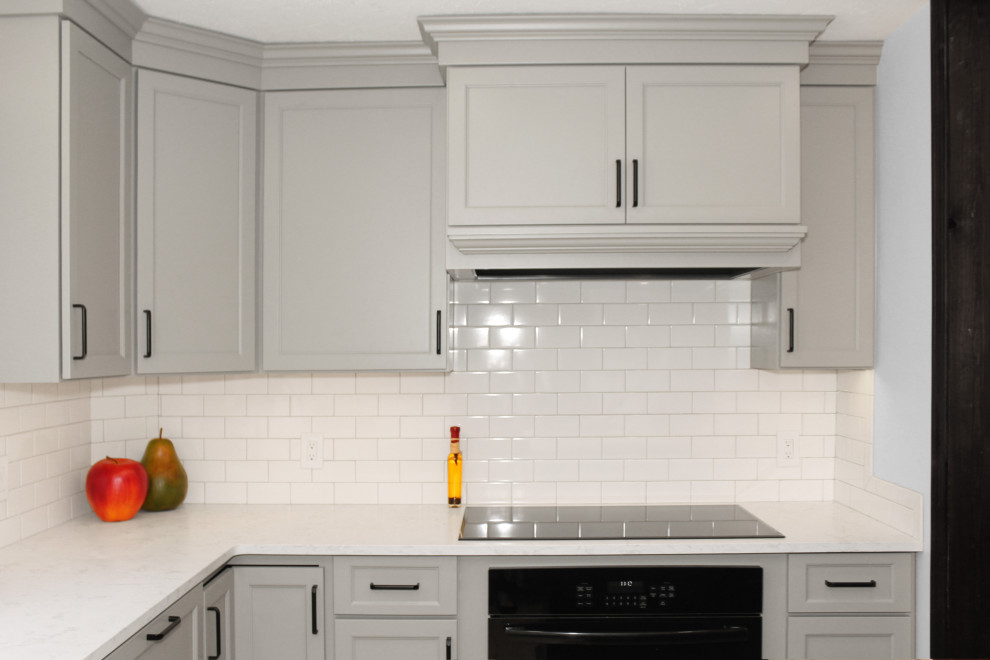 Inspiration for a large transitional u-shaped light wood floor and brown floor enclosed kitchen remodel in Boston with a double-bowl sink, shaker cabinets, gray cabinets, quartz countertops, white backsplash, porcelain backsplash, black appliances, an island and white countertops