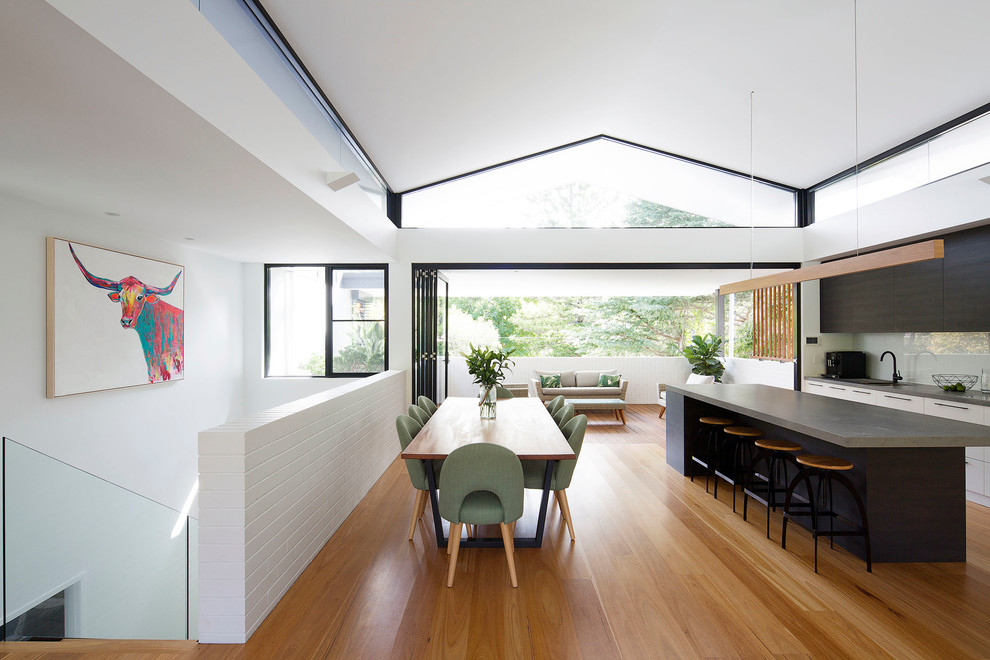 Inspiration for a mid-sized contemporary galley open plan kitchen in Sydney with an undermount sink, flat-panel cabinets, white cabinets, quartz benchtops, white splashback, glass sheet splashback, black appliances, medium hardwood floors, with island, brown floor and grey benchtop.