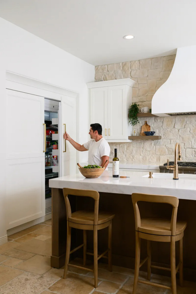 Example of a transitional u-shaped travertine floor and beige floor eat-in kitchen design in Orange County with a farmhouse sink, shaker cabinets, white cabinets, quartz countertops, multicolored backsplash, stone tile backsplash, stainless steel appliances, an island and white countertops
