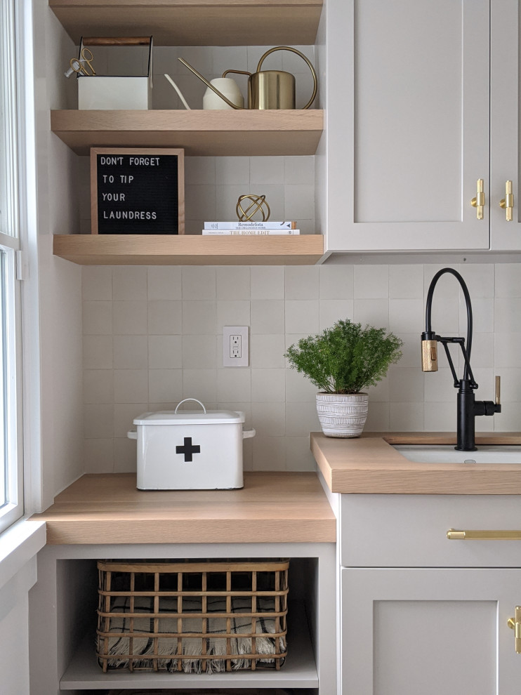 Design ideas for a transitional single-wall dedicated laundry room in Other with an undermount sink, shaker cabinets, beige cabinets, wood benchtops, white splashback, cement tile splashback, white walls, concrete floors, a stacked washer and dryer, multi-coloured floor and beige benchtop.