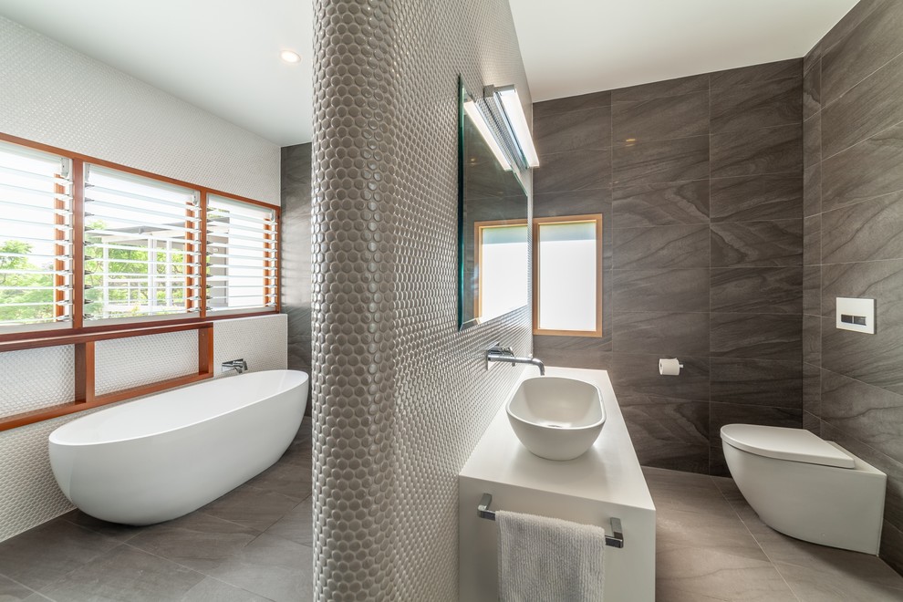 Photo of a large contemporary master bathroom in Sydney with flat-panel cabinets, dark wood cabinets, a freestanding tub, an open shower, a wall-mount toilet, black and white tile, porcelain tile, white walls, porcelain floors, a console sink, solid surface benchtops, grey floor, an open shower and white benchtops.