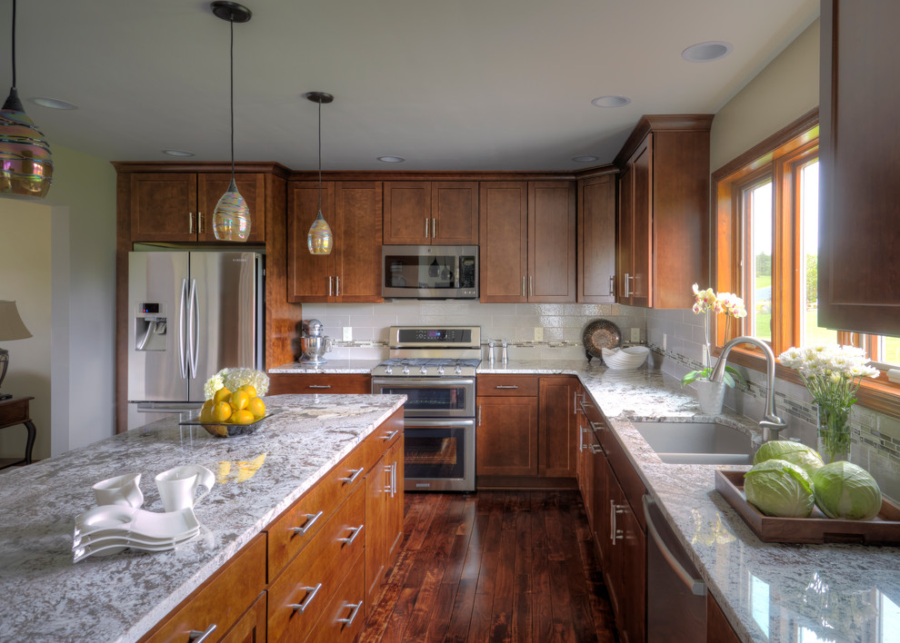 Enclosed kitchen - large transitional l-shaped dark wood floor enclosed kitchen idea in Milwaukee with a drop-in sink, shaker cabinets, medium tone wood cabinets, granite countertops, white backsplash, porcelain backsplash, stainless steel appliances and an island