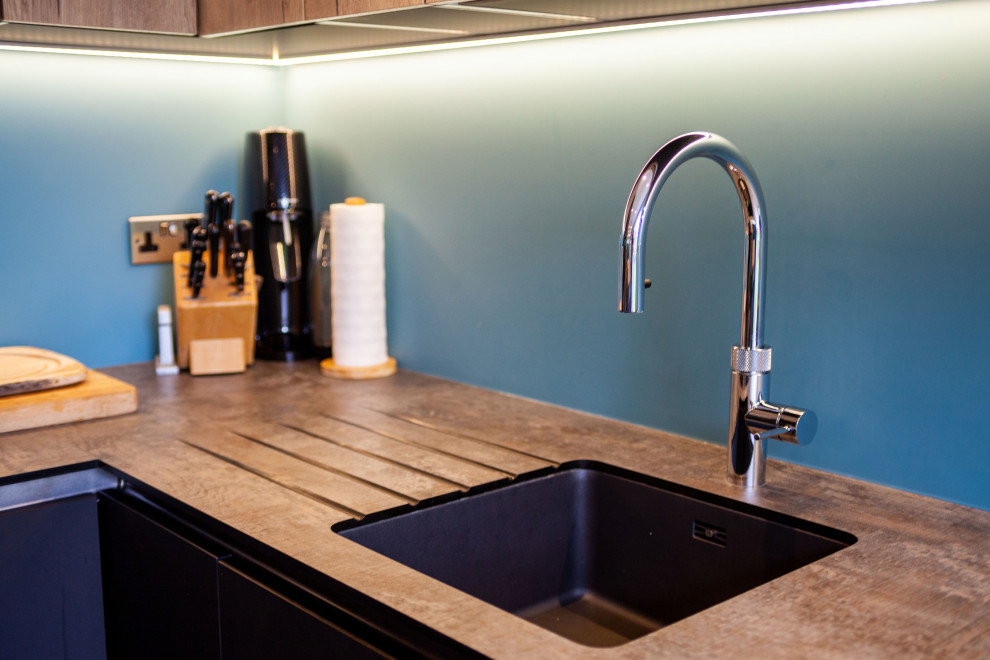 Exempel på ett mellanstort modernt kök med öppen planlösning, med en enkel diskho, släta luckor, blått stänkskydd, glaspanel som stänkskydd och svarta vitvaror