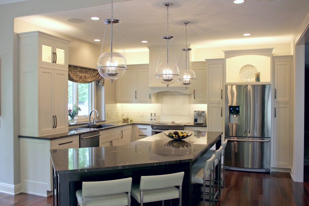 Example of a mid-sized transitional l-shaped dark wood floor eat-in kitchen design with a double-bowl sink, shaker cabinets, white cabinets, granite countertops, white backsplash, glass tile backsplash, stainless steel appliances and an island