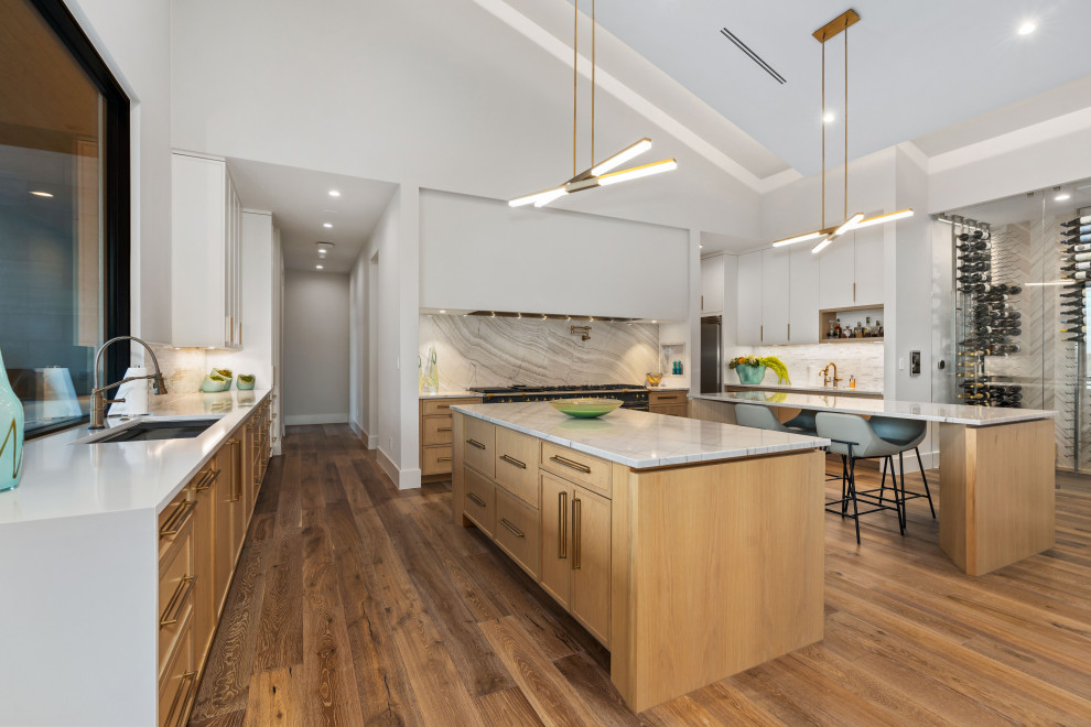 Inspiration for a large kitchen remodel with light wood cabinets, white backsplash, stone slab backsplash, stainless steel appliances, two islands and white countertops