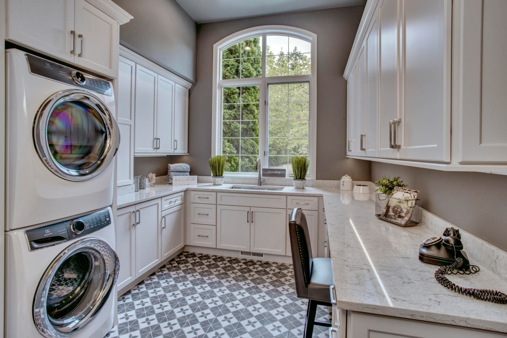 Mid-sized contemporary u-shaped utility room in Seattle with an undermount sink, recessed-panel cabinets, white cabinets, quartzite benchtops, grey walls, porcelain floors, a stacked washer and dryer, grey floor and white benchtop.