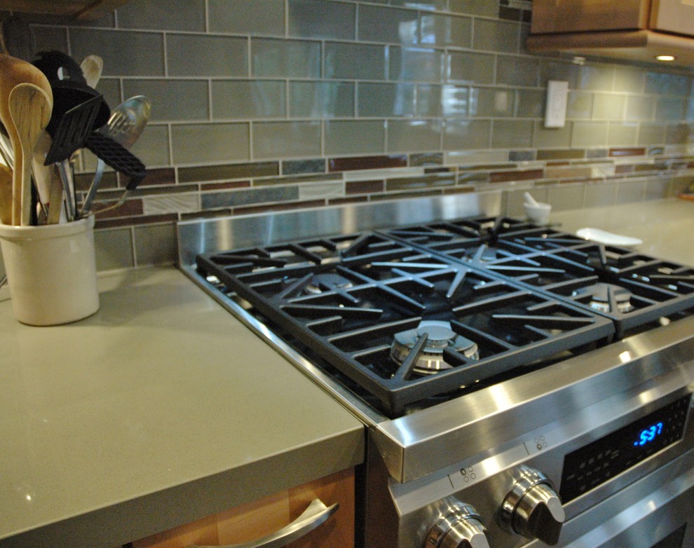 Inspiration for a mid-sized transitional u-shaped slate floor eat-in kitchen remodel in Orange County with glass-front cabinets, light wood cabinets, quartz countertops, green backsplash, glass tile backsplash, stainless steel appliances and an island