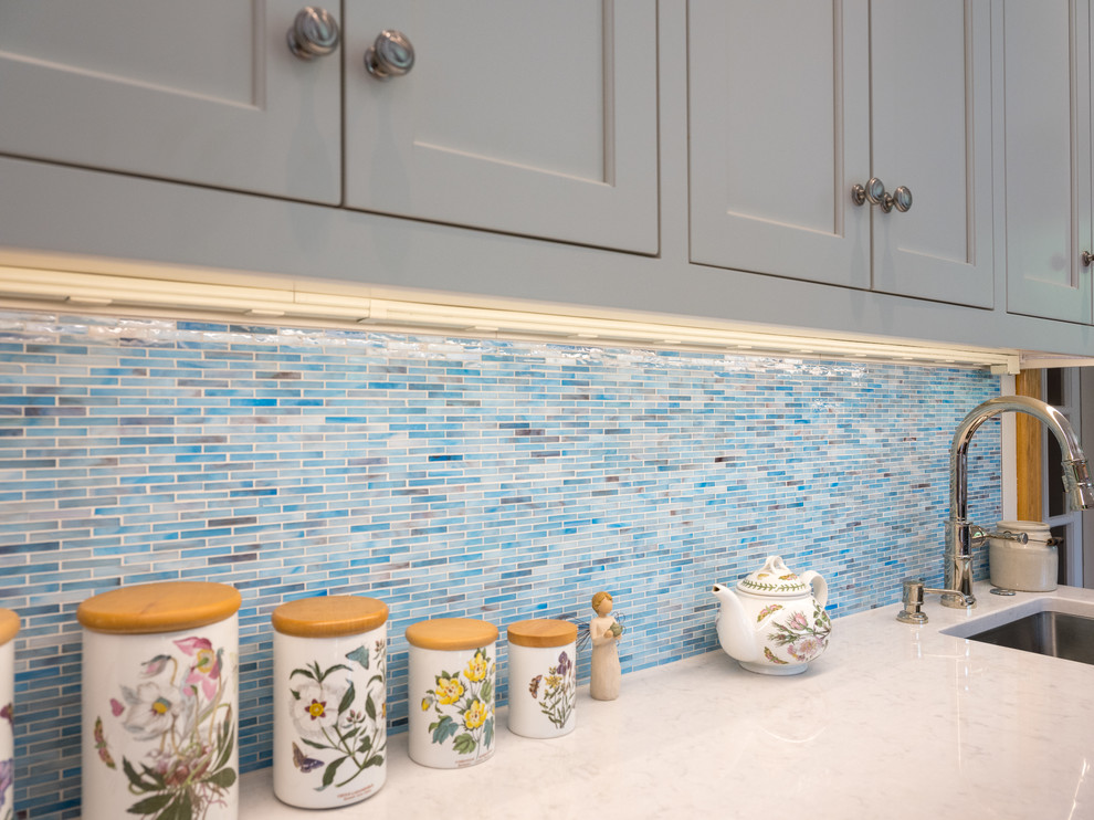 This is an example of a large traditional l-shaped open plan kitchen in Philadelphia with an undermount sink, flat-panel cabinets, white cabinets, blue splashback, glass tile splashback, white appliances, light hardwood floors, with island and blue floor.