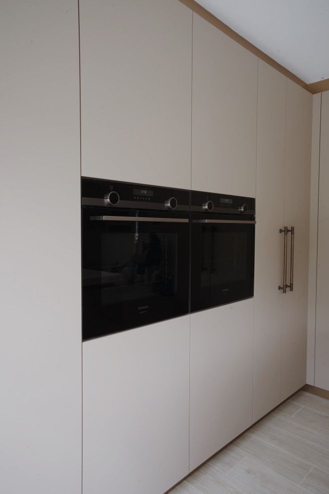 Inspiration for a medium sized modern l-shaped enclosed kitchen in London with a built-in sink, flat-panel cabinets, beige cabinets, quartz worktops, light hardwood flooring, an island, beige floors and beige worktops.