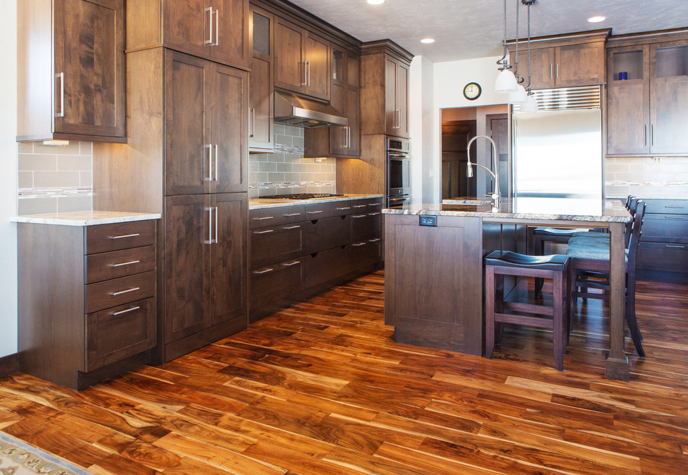 Large transitional l-shaped dark wood floor and brown floor open concept kitchen photo with a farmhouse sink, shaker cabinets, dark wood cabinets, granite countertops, beige backsplash, subway tile backsplash, stainless steel appliances and an island