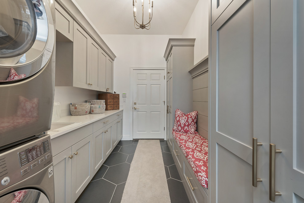 Mid-sized country single-wall utility room in Salt Lake City with shaker cabinets, grey cabinets, quartzite benchtops, ceramic floors, a stacked washer and dryer, black floor, beige benchtop, an undermount sink and white walls.