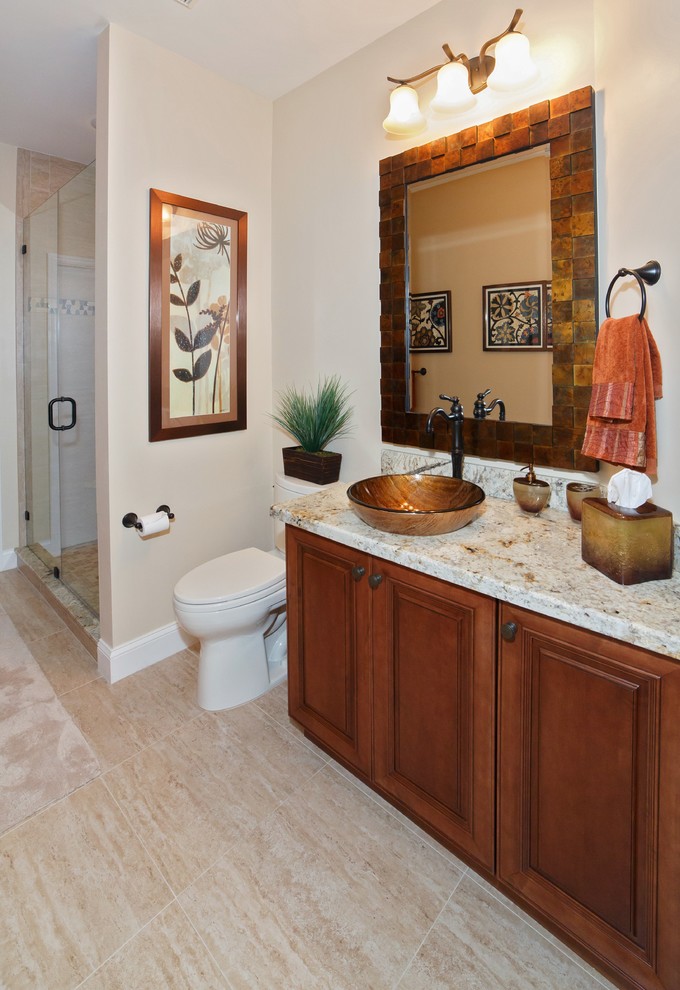 This is an example of a mid-sized transitional bathroom in Miami with a vessel sink, raised-panel cabinets, medium wood cabinets, granite benchtops, an alcove shower, a one-piece toilet, beige tile, cement tile, beige walls and ceramic floors.