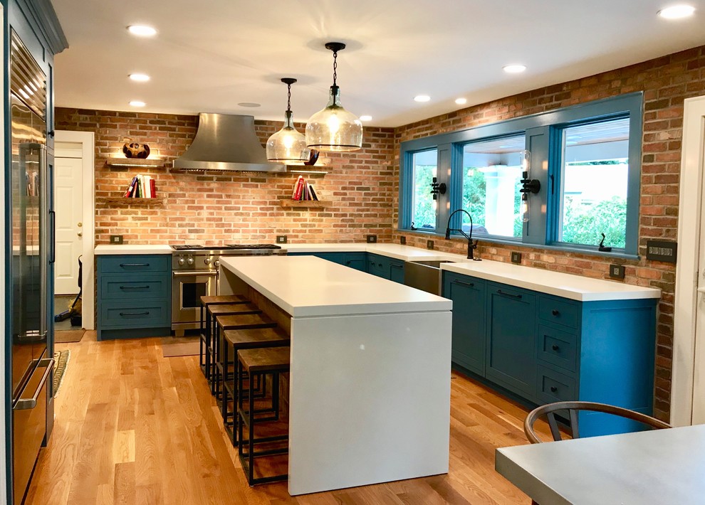 Example of a large mountain style l-shaped medium tone wood floor and brown floor eat-in kitchen design with a farmhouse sink, flat-panel cabinets, blue cabinets, concrete countertops, red backsplash, brick backsplash, stainless steel appliances, an island and white countertops