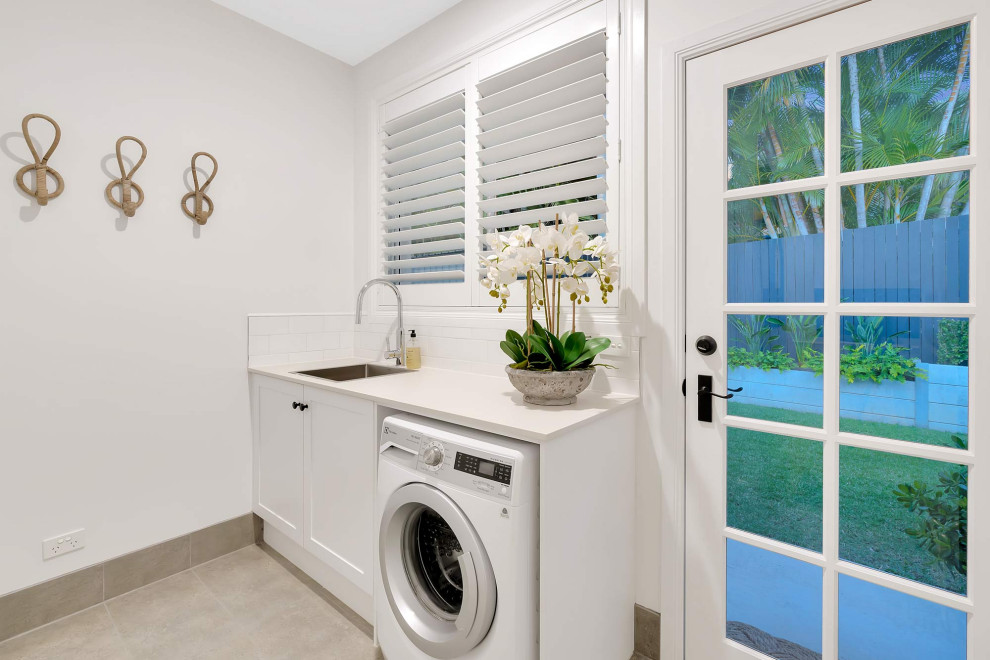 Photo of a mid-sized beach style galley laundry room in Gold Coast - Tweed with shaker cabinets, turquoise cabinets, quartz benchtops, white splashback, subway tile splashback, white walls, ceramic floors, beige floor and white benchtop.