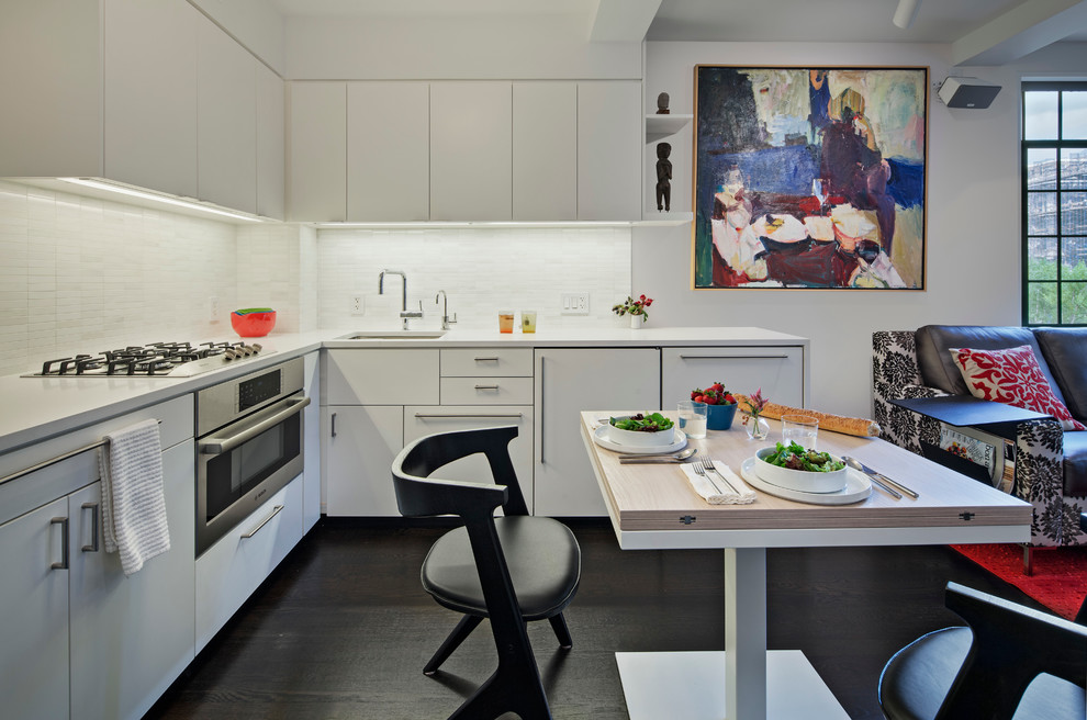 Inspiration for a mid-sized modern l-shaped eat-in kitchen in New York with an undermount sink, flat-panel cabinets, white cabinets, terrazzo benchtops, white splashback, ceramic splashback, white appliances, dark hardwood floors and no island.