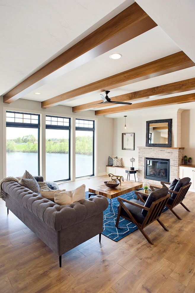 Mid-sized transitional open concept living room in Other with grey walls, laminate floors, a standard fireplace, a brick fireplace surround, a wall-mounted tv and brown floor.