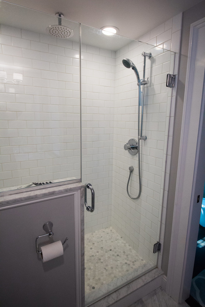 Example of a mid-sized transitional master travertine floor corner shower design in Boston with shaker cabinets, white cabinets, a two-piece toilet, gray walls, an undermount sink and solid surface countertops