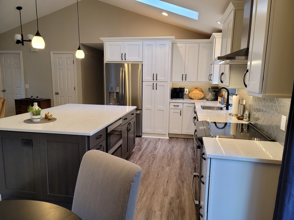 Inspiration for a l-shaped laminate floor, brown floor and vaulted ceiling eat-in kitchen remodel in Seattle with an undermount sink, shaker cabinets, white cabinets, quartz countertops, gray backsplash, glass tile backsplash, stainless steel appliances, an island and multicolored countertops