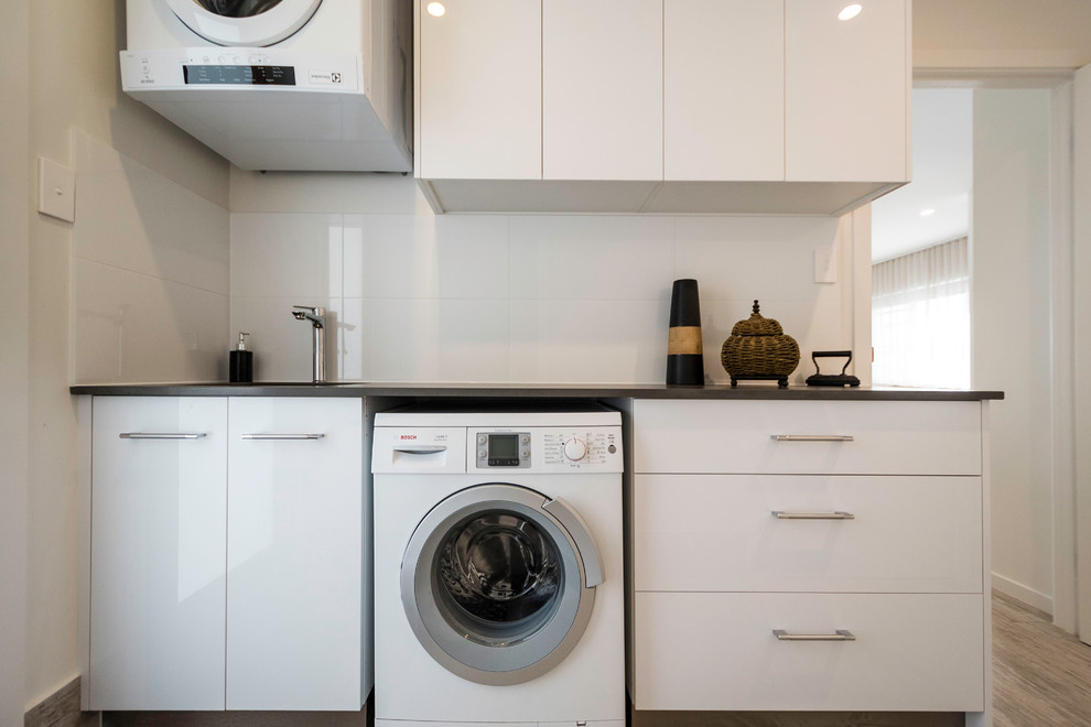 Design ideas for a mid-sized contemporary single-wall dedicated laundry room in Gold Coast - Tweed with an undermount sink, flat-panel cabinets, quartz benchtops, a stacked washer and dryer and beige walls.