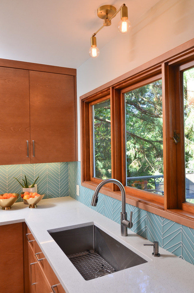 Photo of a mid-sized midcentury u-shaped eat-in kitchen in Portland with an undermount sink, flat-panel cabinets, medium wood cabinets, quartz benchtops, blue splashback, glass tile splashback, stainless steel appliances, light hardwood floors, a peninsula and white benchtop.