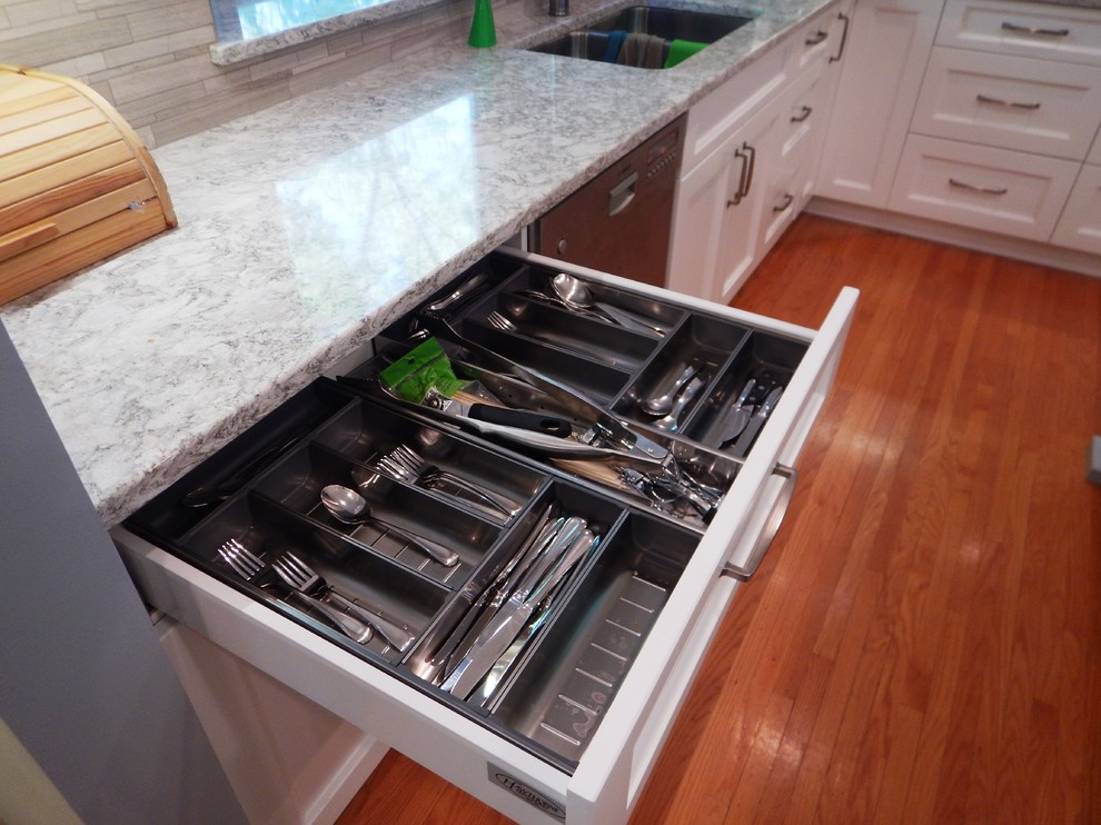 Large transitional l-shaped light wood floor eat-in kitchen photo with an undermount sink, recessed-panel cabinets, white cabinets, quartz countertops, gray backsplash, stone tile backsplash, stainless steel appliances and an island