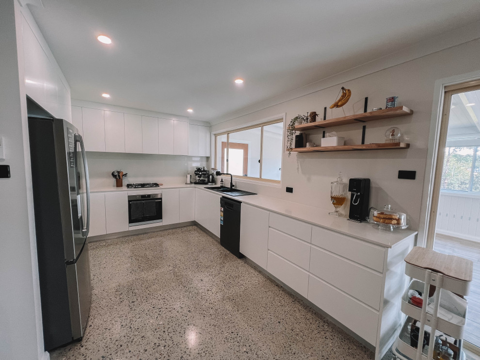 Bild på ett litet nordiskt vit vitt kök, med en dubbel diskho, släta luckor, vita skåp, bänkskiva i kvarts, vitt stänkskydd, svarta vitvaror, betonggolv och grått golv
