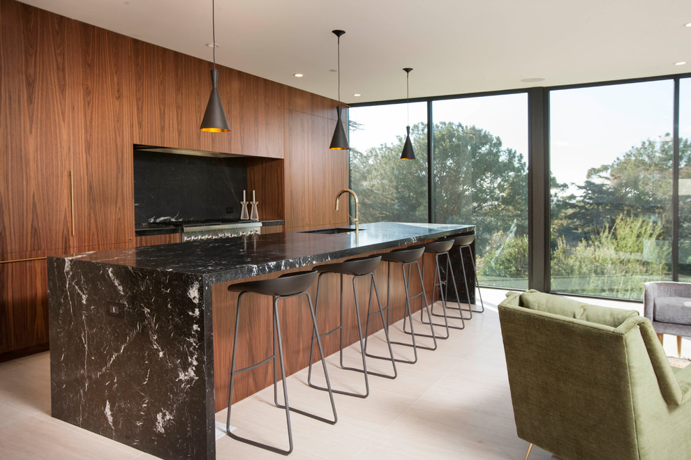 Contemporary galley open plan kitchen in San Diego with an undermount sink, flat-panel cabinets, medium wood cabinets, marble benchtops, black splashback, marble splashback, stainless steel appliances, with island, white floor and black benchtop.