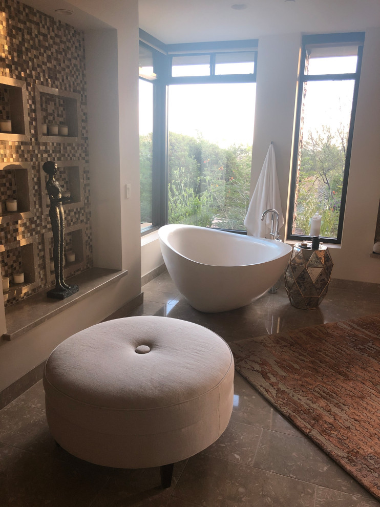 This is an example of an expansive contemporary master bathroom in Phoenix with flat-panel cabinets, light wood cabinets, a freestanding tub, an open shower, a one-piece toilet, multi-coloured tile, glass sheet wall, white walls, limestone floors, a drop-in sink, limestone benchtops, green floor, beige benchtops, a laundry, a double vanity and a built-in vanity.
