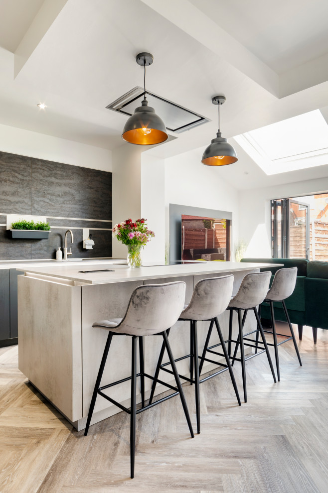 Photo of a mid-sized modern l-shaped open plan kitchen in Manchester with an undermount sink, flat-panel cabinets, grey cabinets, laminate benchtops, brown splashback, black appliances, light hardwood floors, with island, beige floor, grey benchtop and vaulted.