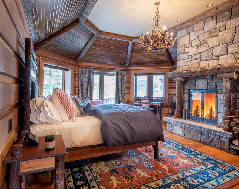 This is an example of a large country master bedroom in Burlington with brown walls, medium hardwood floors, a standard fireplace, a stone fireplace surround and brown floor.