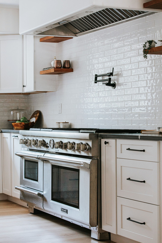 Inspiration for a large country galley eat-in kitchen in Denver with a farmhouse sink, shaker cabinets, white cabinets, granite benchtops, white splashback, subway tile splashback, stainless steel appliances, with island, beige floor, black benchtop and exposed beam.