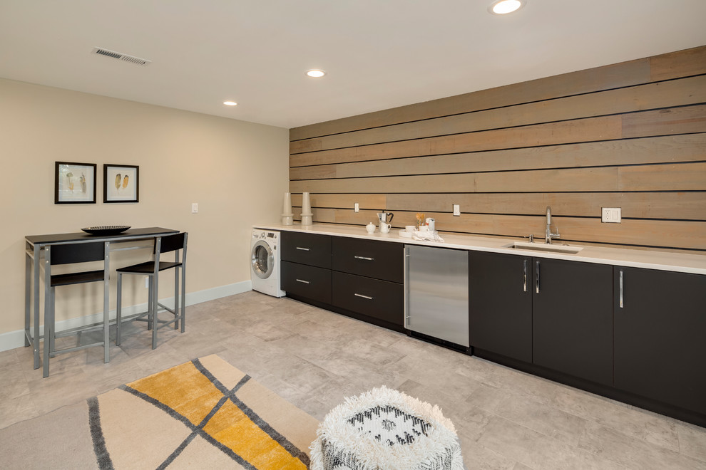Inspiration for a mid-sized contemporary single-wall utility room in Los Angeles with an undermount sink, flat-panel cabinets, black cabinets, solid surface benchtops, beige walls, ceramic floors, a side-by-side washer and dryer and beige floor.