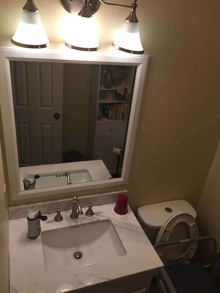 Small transitional vinyl floor home design photo with white cabinets, a two-piece toilet, beige walls, an undermount sink, marble countertops and raised-panel cabinets