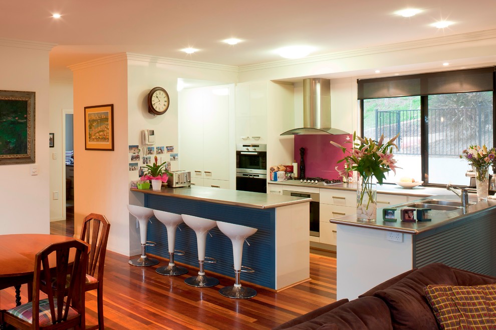 Photo of a mid-sized modern galley open plan kitchen in Brisbane with a double-bowl sink, flat-panel cabinets, beige cabinets, laminate benchtops, pink splashback, glass tile splashback, stainless steel appliances, medium hardwood floors and with island.