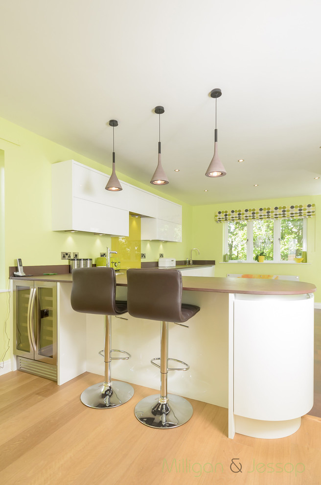 Mid-sized contemporary l-shaped eat-in kitchen in Manchester with white cabinets, solid surface benchtops, green splashback, glass sheet splashback and stainless steel appliances.